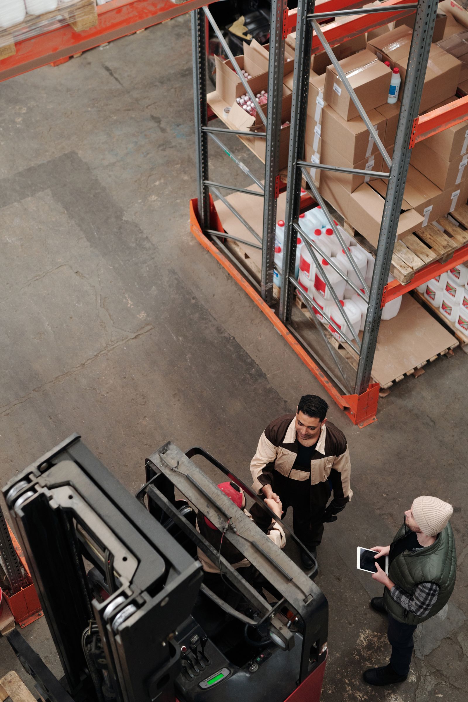 Warehouse employees discussing work beside a forklift and storage racks