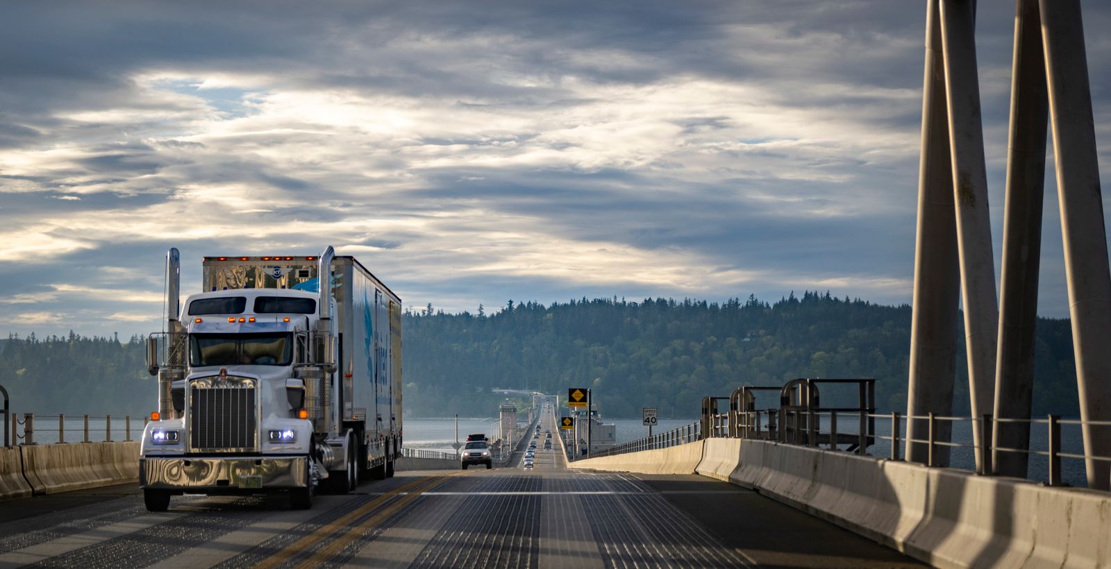 American semi-truck crossing a bridge with a forested landscape behind it